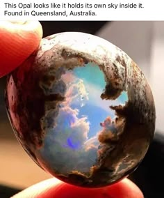 a hand holding a marble ball with clouds reflected in it