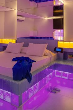 a large bed sitting under a purple light next to a wall filled with mirrors and lights