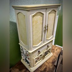 a white cabinet with floral designs painted on the doors and drawers is sitting on a wooden table