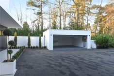 an empty garage with trees in the background and bushes on the ground next to it