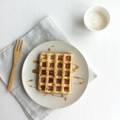 a plate with waffles on it next to a fork and cup of sugar