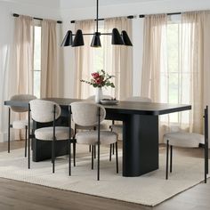 a dining room table with four chairs and a vase on the table in front of two windows