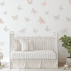 a white crib in front of a wall with pink butterflies on it and a potted plant