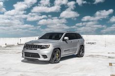 a silver jeep parked on top of a snow covered parking lot next to a white fence