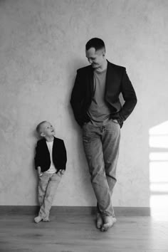 a man standing next to a little boy in front of a wall with his hands on his hips