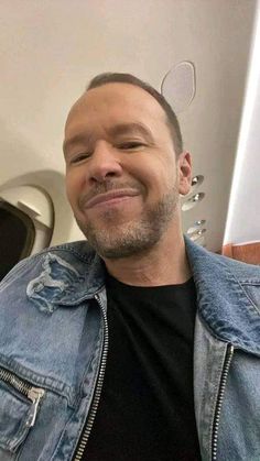 a man in a denim jacket smiles at the camera while wearing ears on his head