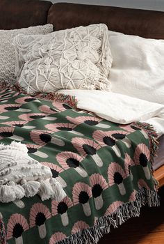 a bed covered in blankets and pillows on top of a wooden floor next to a brown couch