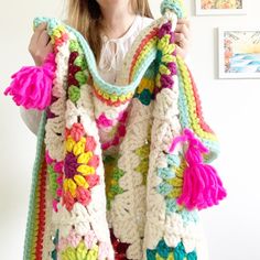 a woman holding up a colorful crocheted scarf