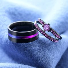 two wedding bands with pink and purple stones on them sitting next to each other in front of a blue blanket