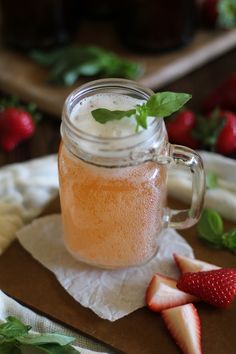 a mason jar filled with liquid next to sliced strawberries and basil leaves on a napkin