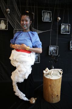 a woman standing in front of a black backdrop with pictures on the wall and hanging from strings