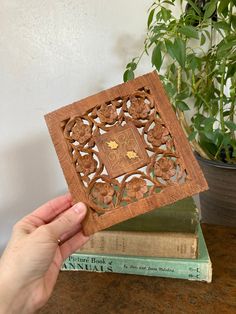 a person is holding up a carved wooden book with an intricate design on the cover