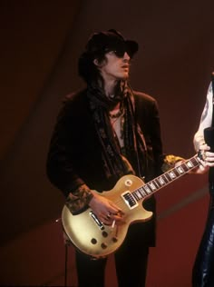 two people standing next to each other with guitars in their hands and one person holding an electric guitar