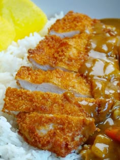 a plate with rice, meat and gravy next to a slice of lemon