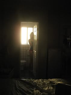 a woman standing in the doorway of a dark room with sunlight coming through the window