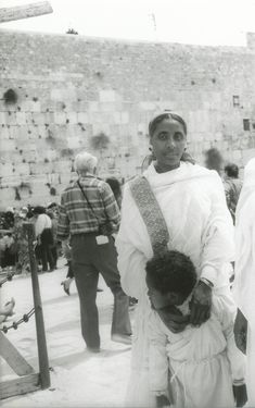 an old black and white photo of people in front of a stone wall with crosses on it