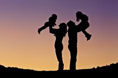 the silhouette of two people and a child against a purple sky at sunset or dawn