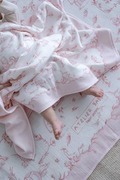 a baby wrapped in a pink blanket laying on top of a white and pink bed