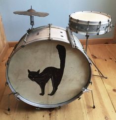 a black cat painted on the side of a drum set in a room with wood floors