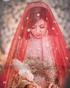 a woman wearing a red veil and holding a flower in her hand with the background blurred out