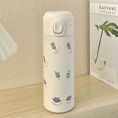 thermos bottle is sitting next to a plant on a shelf near a lamp