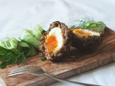 an egg in the middle of some meat on a wooden cutting board with a fork