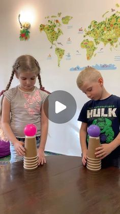 two young children standing at a table with cups in front of them