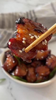 a bowl filled with meat and chopsticks sitting on top of a white table