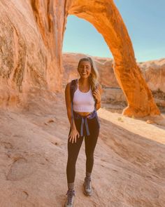 a woman standing in front of a rock formation with her hands on her hips and smiling at the camera