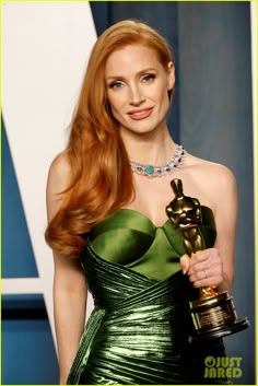 a woman with long red hair holding an award in front of a blue wall and wearing a green dress