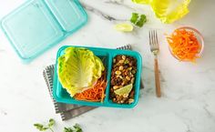 two plastic trays filled with food on top of a white marble counter next to utensils