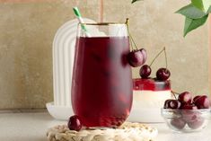 a glass filled with liquid next to some cherries