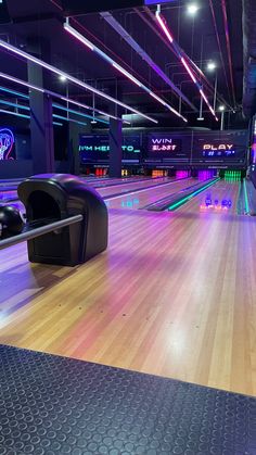 an empty bowling alley with neon lights on the walls and wood flooring at night