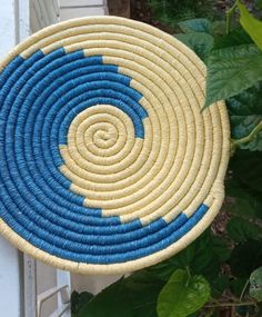 a blue and yellow woven basket hanging on a wall next to green leaves in front of a white door