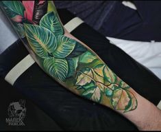 a man's arm with green leaves and flowers on it