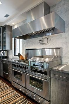 a kitchen with stainless steel appliances and wooden flooring, along with an area rug