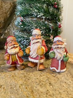 three santa figurines sitting next to a christmas tree