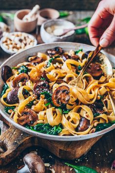 a bowl filled with noodles, mushrooms and spinach on top of a wooden table