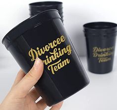 a hand holding a black coffee cup with gold lettering on it and three other cups in the background