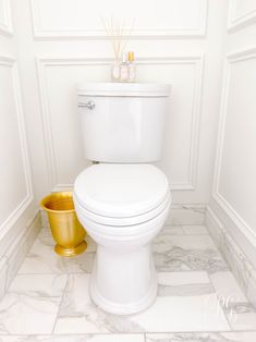 a white toilet sitting in a bathroom next to a yellow trash can and gold cup