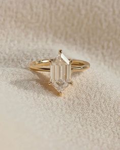 a gold ring with an emerald cut diamond in the center on a white cloth background