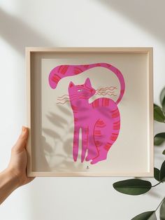 a person holding up a pink paper cut art piece with a cat on it's back