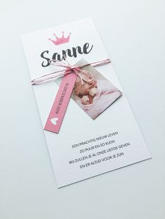 a baby announcement card with a pink ribbon tied around it and a crown on top