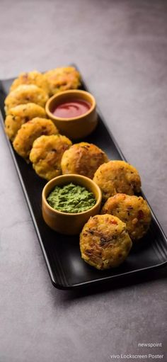 some food is on a black plate with sauces and dips in small bowls