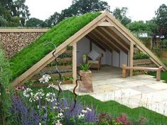 a house with a green roof covered in grass and flowers next to a wooden bench