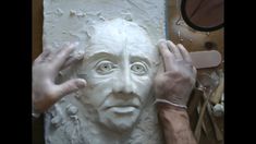 two hands are working on a clay face that is being sculpted into a man's head