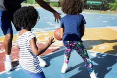 a man and two children playing basketball on a court with one child holding the ball