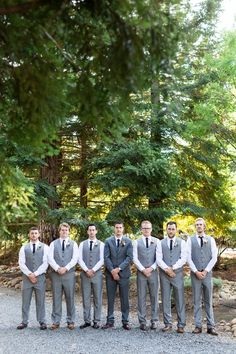 a group of men standing next to each other on top of a gravel road in front of trees