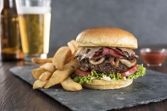 a hamburger and fries on a slate board with a glass of beer in the background