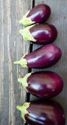 three eggplant's are lined up on a wooden surface